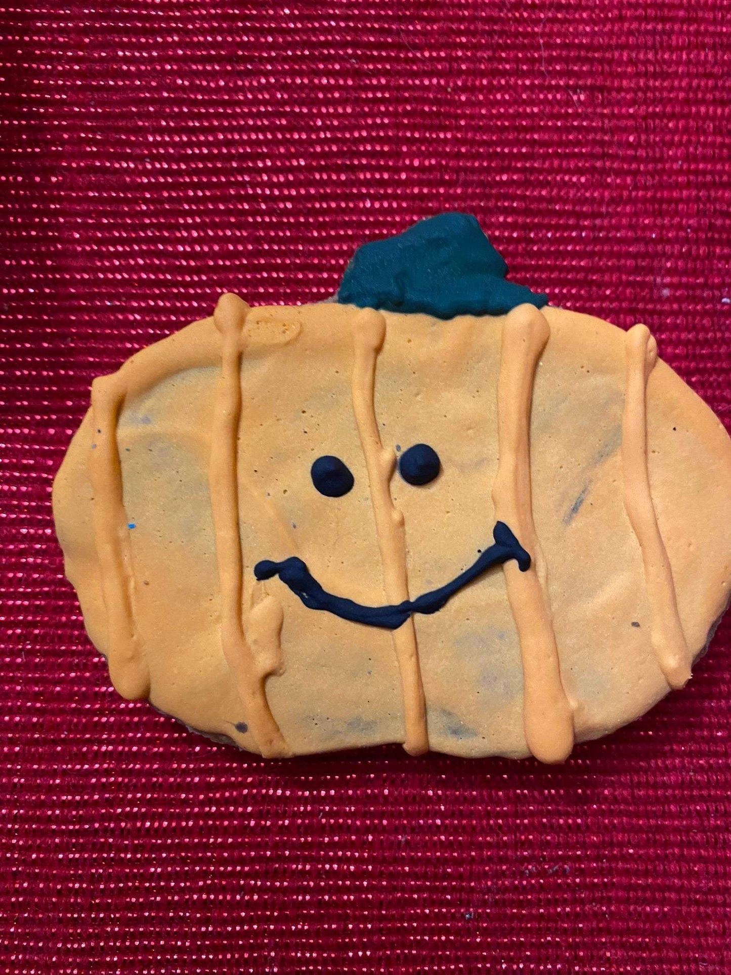 Organic Halloween dog cookie shaped like a pumpkin with smiling face on red background