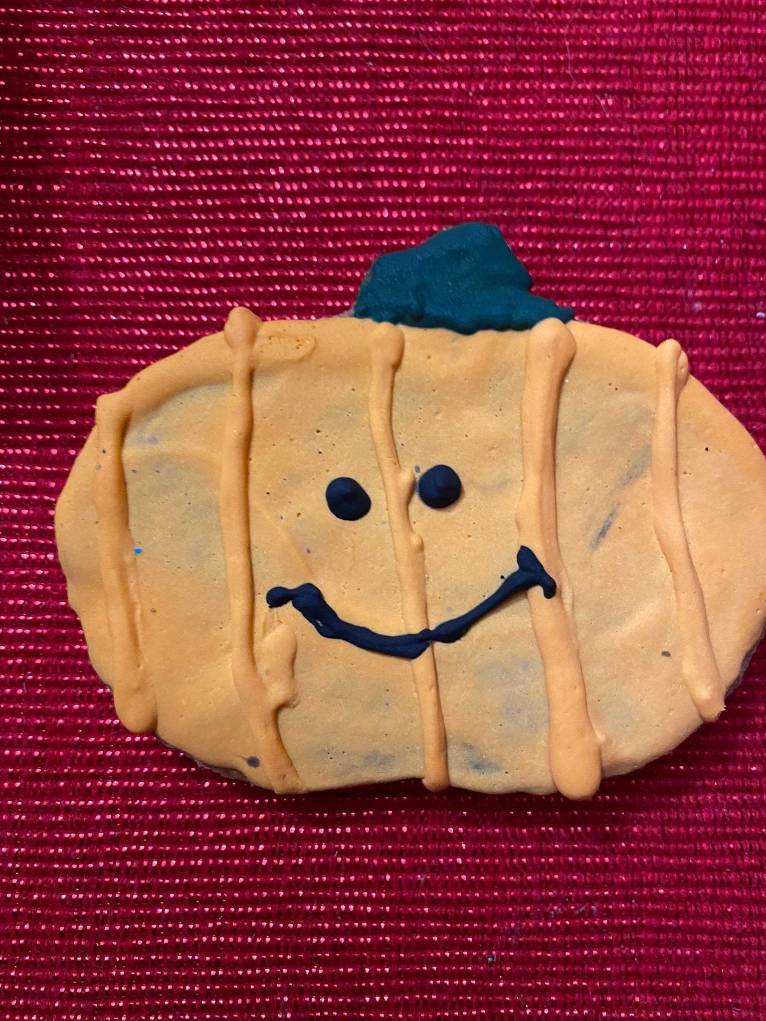 Organic Halloween dog cookie shaped like a pumpkin with smiling face on red background