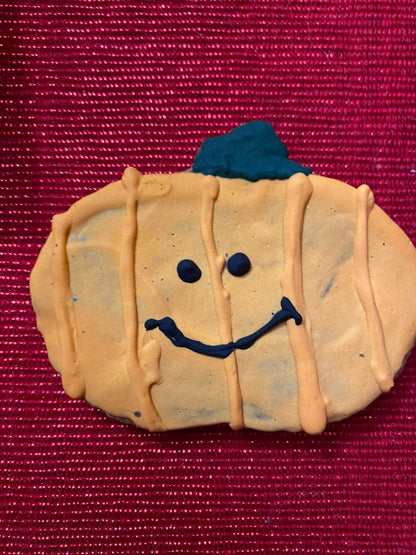 Organic Halloween dog cookie shaped like a pumpkin with smiling face on red background