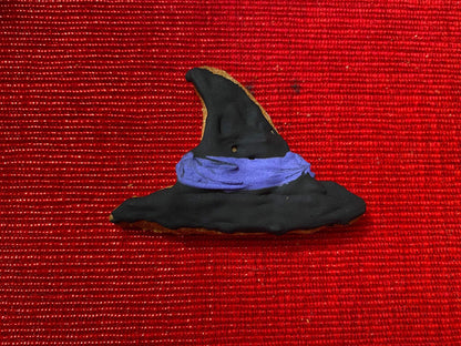 Black witch hat shaped organic Halloween dog cookie with purple icing band on red textured background