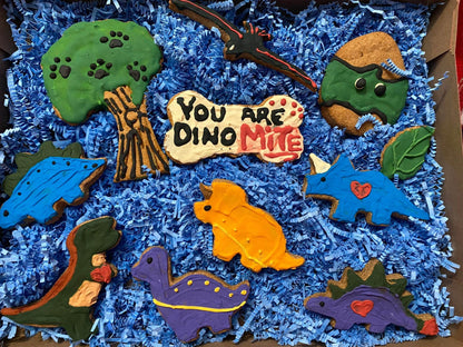 Organic dinosaur-shaped dog cookies in a colorful gift box with a "You Are DinoMite" treat on blue shredded paper