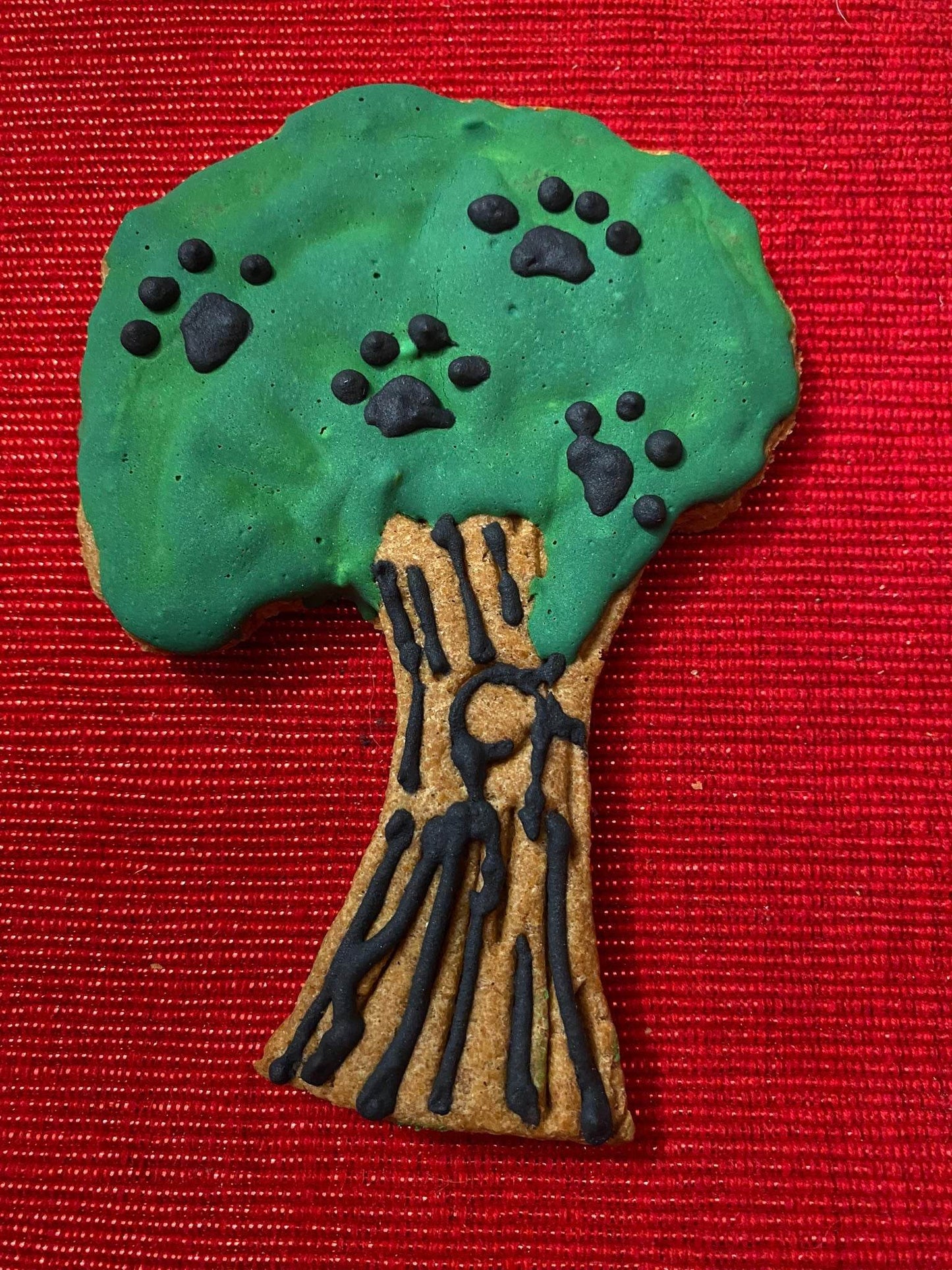 Organic dinosaur-shaped dog cookie decorated green and brown with paw print details on red background