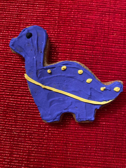 Purple dinosaur-shaped organic dog cookie with yellow icing on red textured background from Dinosaurs Organic Dog Cookie Box