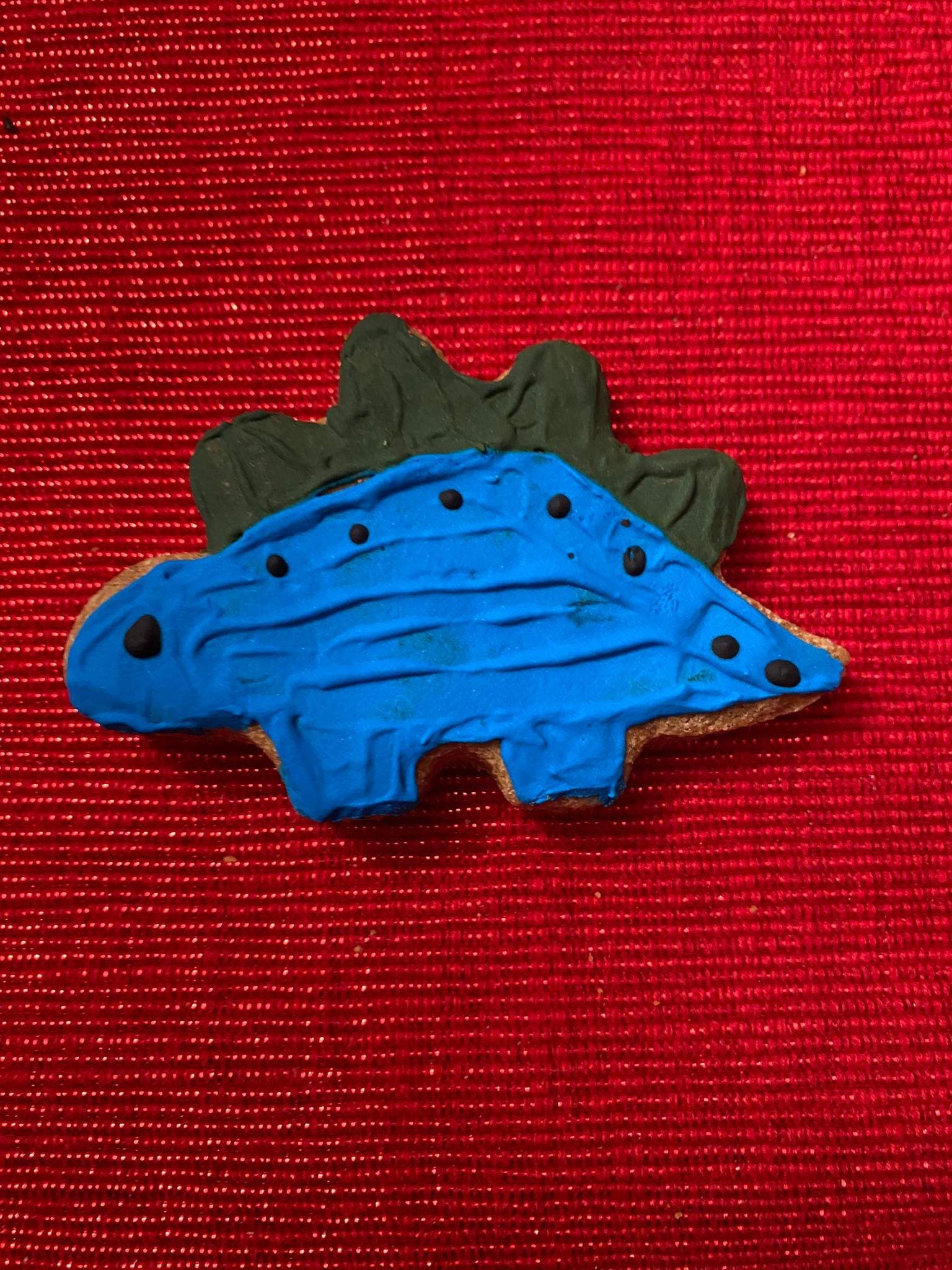 Organic dinosaur-shaped dog cookie with blue icing on red background from Dinosaurs Organic Dog Cookie Box