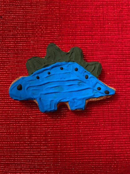 Organic dinosaur-shaped dog cookie with blue icing on red background from Dinosaurs Organic Dog Cookie Box