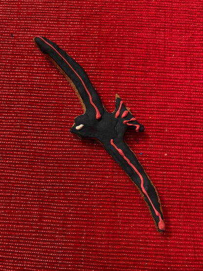 Dinosaur-shaped organic dog cookie on red textured background from Dinosaurs Organic Dog Cookie Box