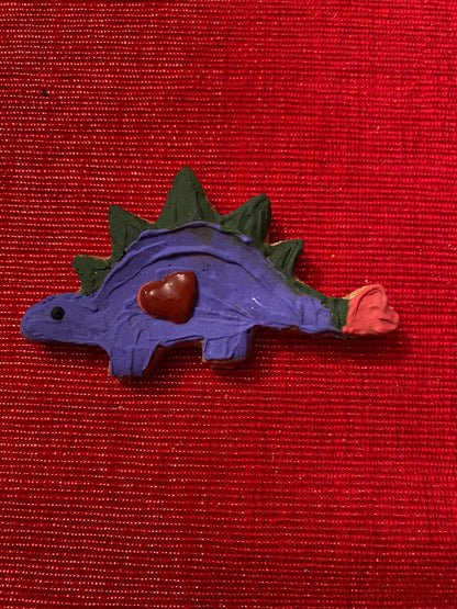 Purple dinosaur-shaped organic dog cookie with a heart decoration on red textured background