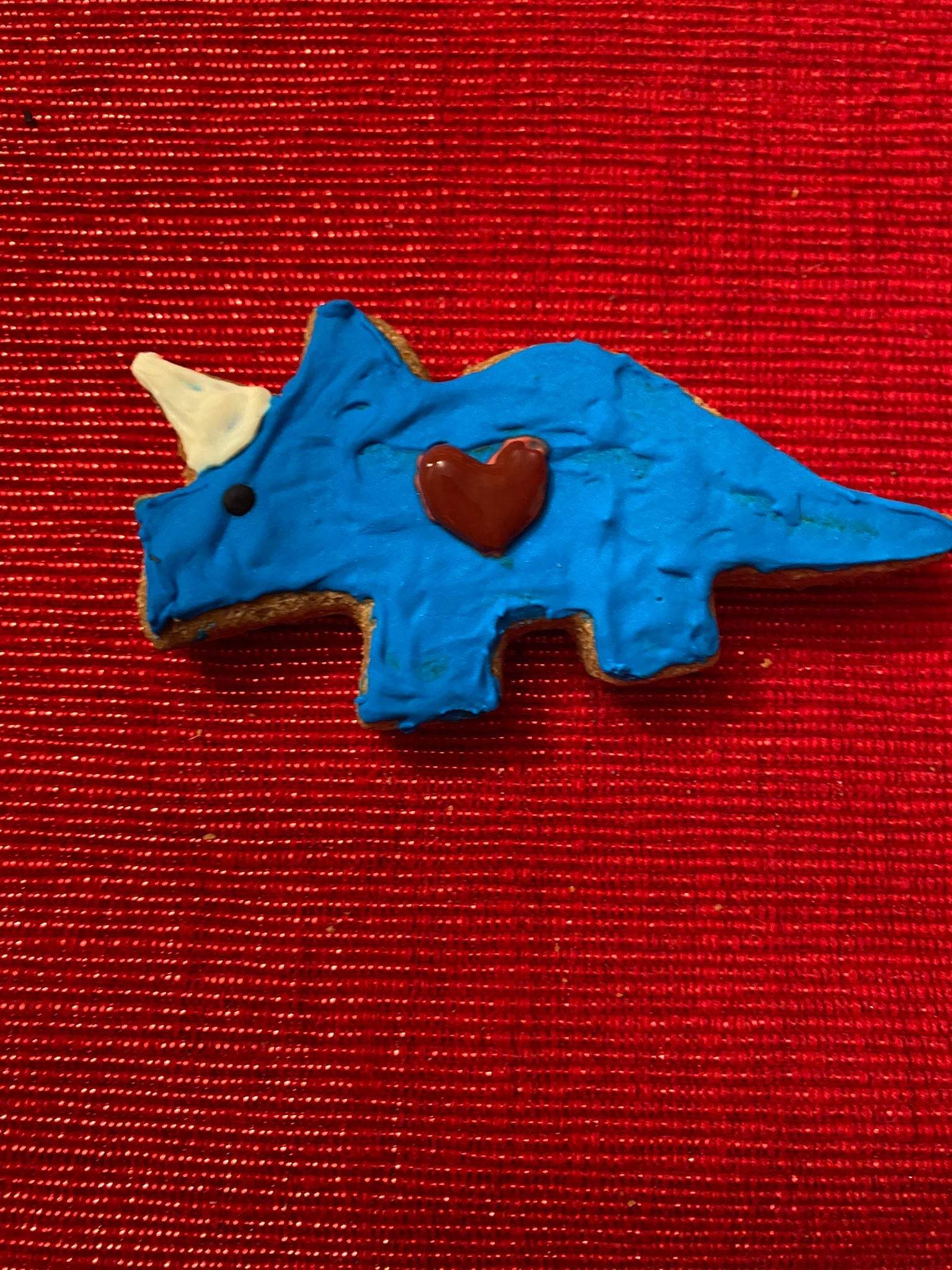 Blue dinosaur-shaped organic dog cookie with a heart decoration on red textured background Dinosaurs Organic Dog Cookie Box