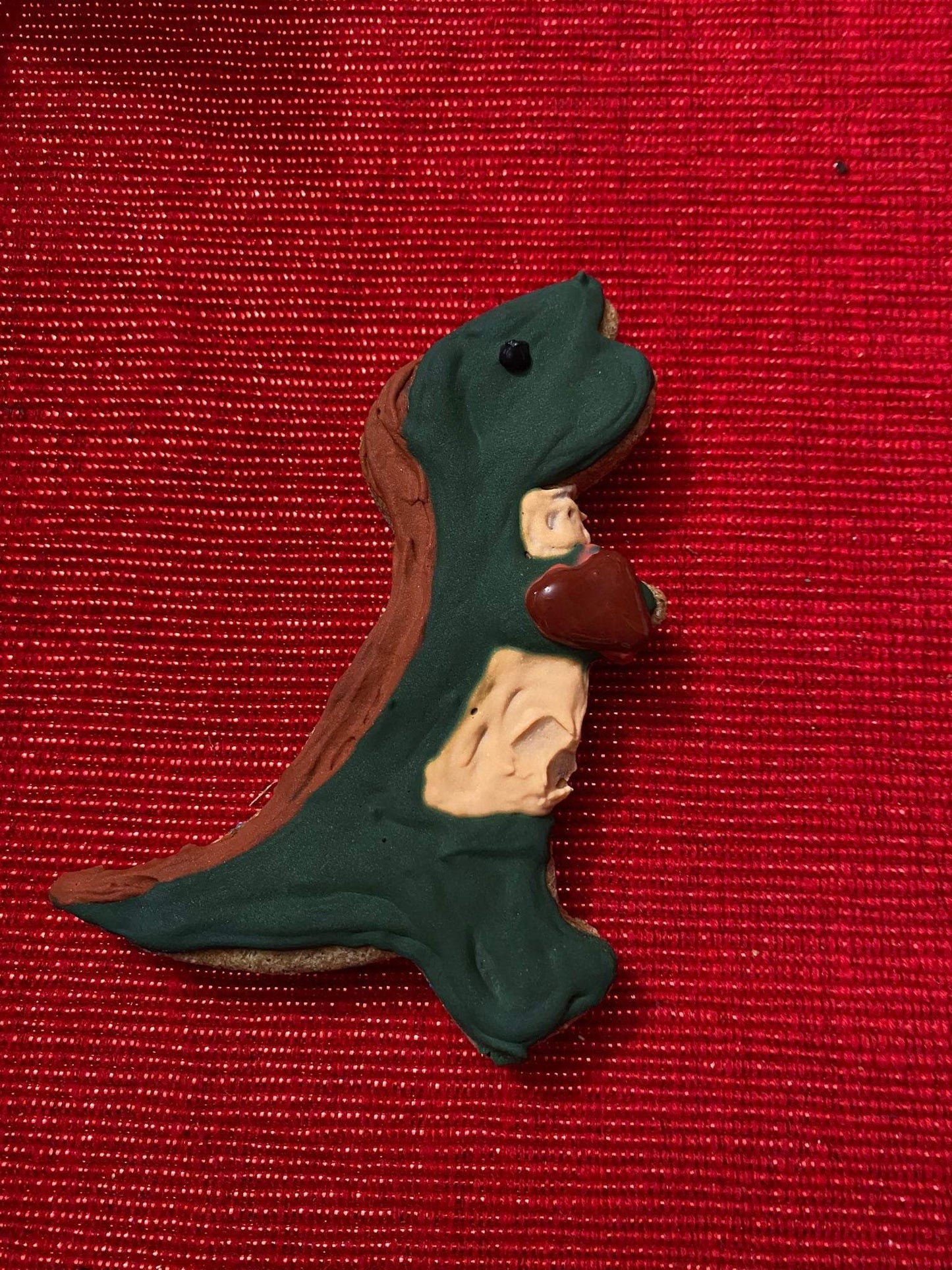 Dinosaur-shaped organic dog cookie with natural ingredients on red background