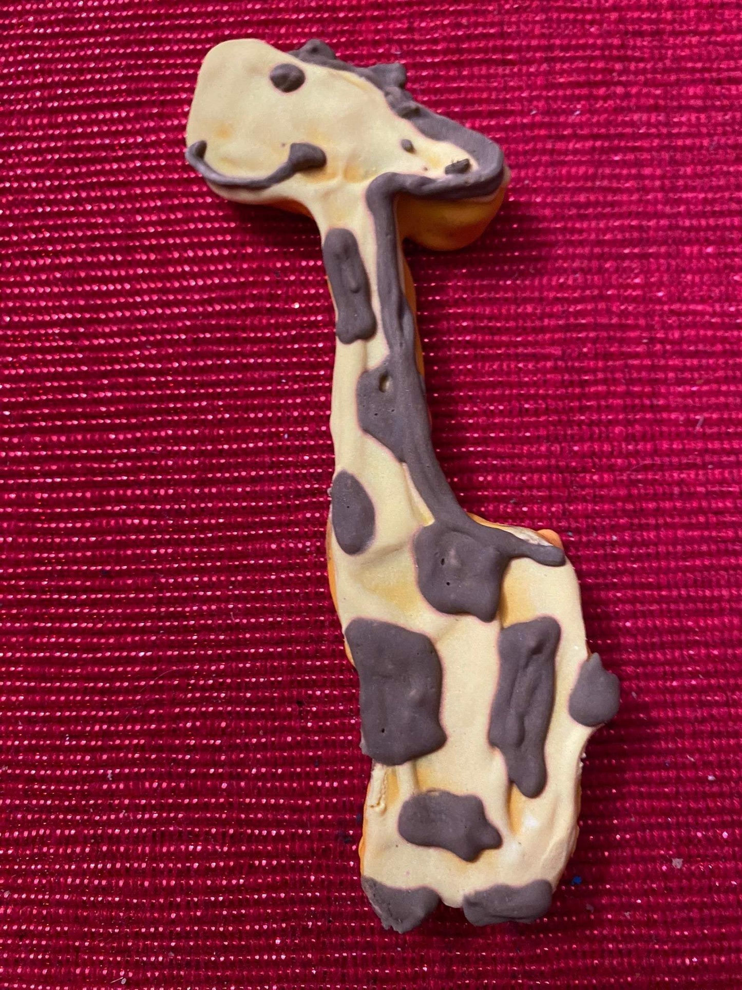 Organic dinosaur-shaped dog cookie with chocolate spots on red background from Dinosaurs Organic Dog Cookie Box