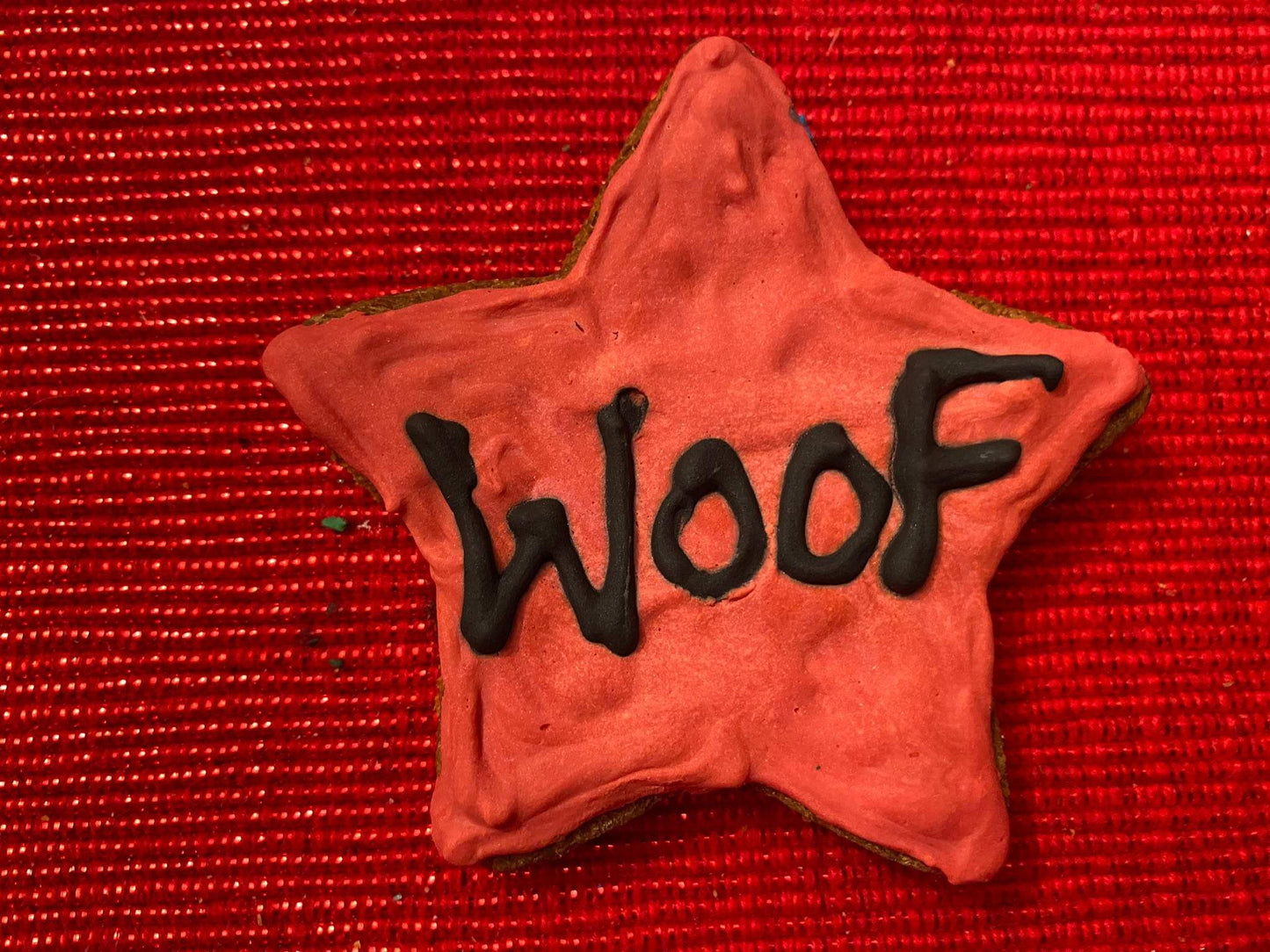 Star-shaped organic dog cookie with red icing and "Woof" written in black icing on red textured background from Dog Life Organic Dog Cookie Box