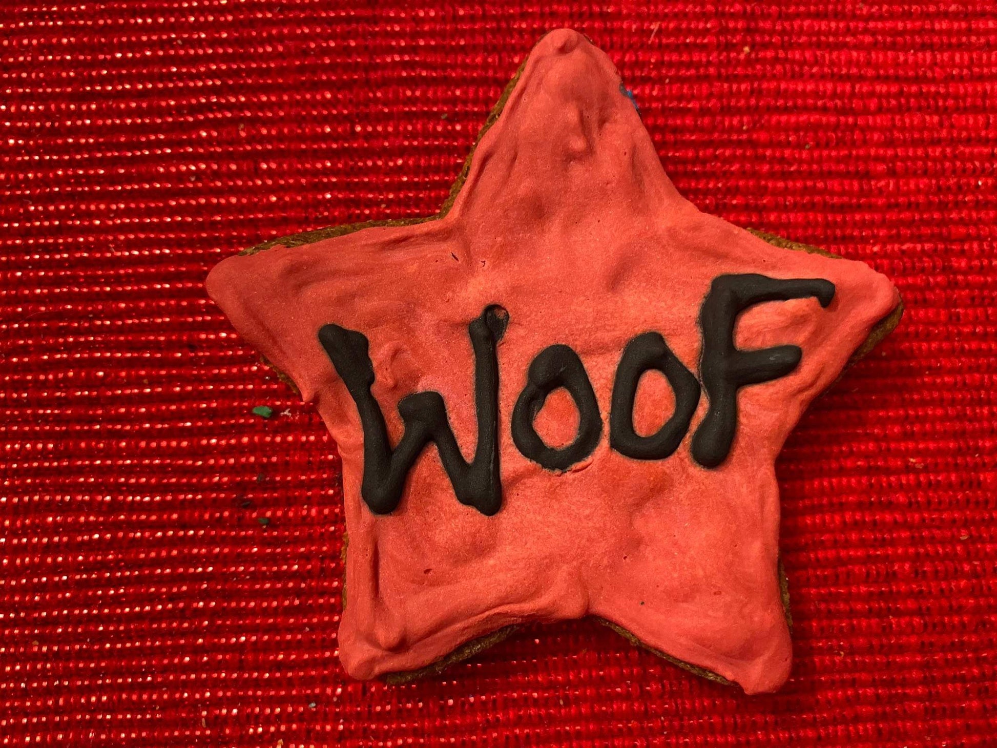 Star-shaped organic dog cookie with red icing and "Woof" written in black icing on red textured background from Dog Life Organic Dog Cookie Box