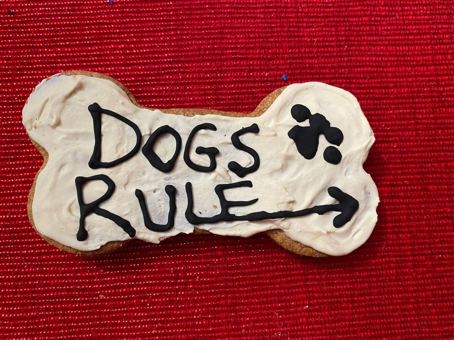 Dog Life Organic Dog Cookie shaped like a bone with "Dogs Rule" text and paw print on white icing against red background