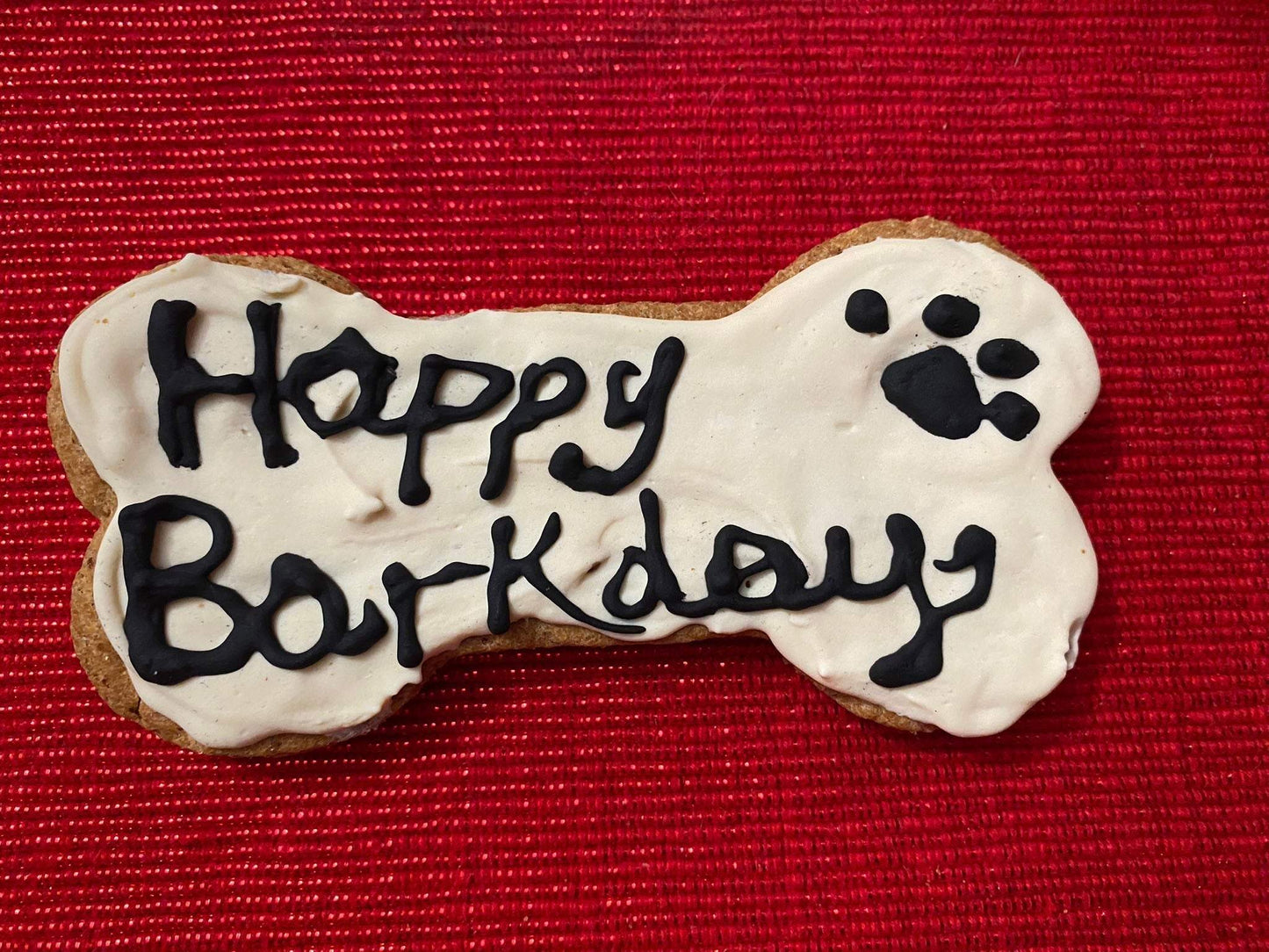 Birthday Girl organic dog cookie bone-shaped with "Happy Barkday" text and paw print on white icing over red textured background