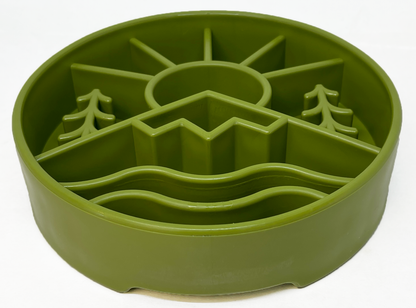 Green slow feeder dog bowl with raised ridges in outdoor nature design featuring sun, mountains, and trees for mental enrichment and slow eating