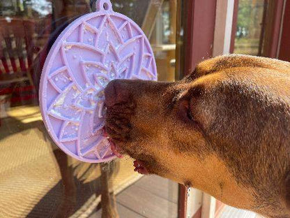 Dog licking a pastel purple lotus design enrichment lick mat with suction cups attached to a glass door