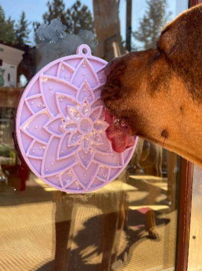 Dog licking pastel purple lotus design enrichment lick mat with suction cups attached to glass window