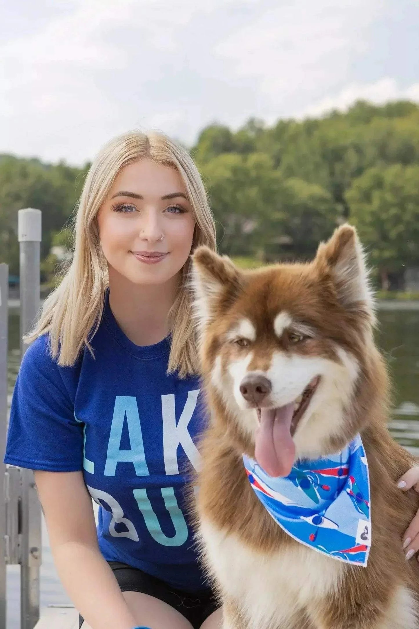 Dog wearing vibrant K9 Kayak Dog Bandana by lakeside with woman in blue shirt.