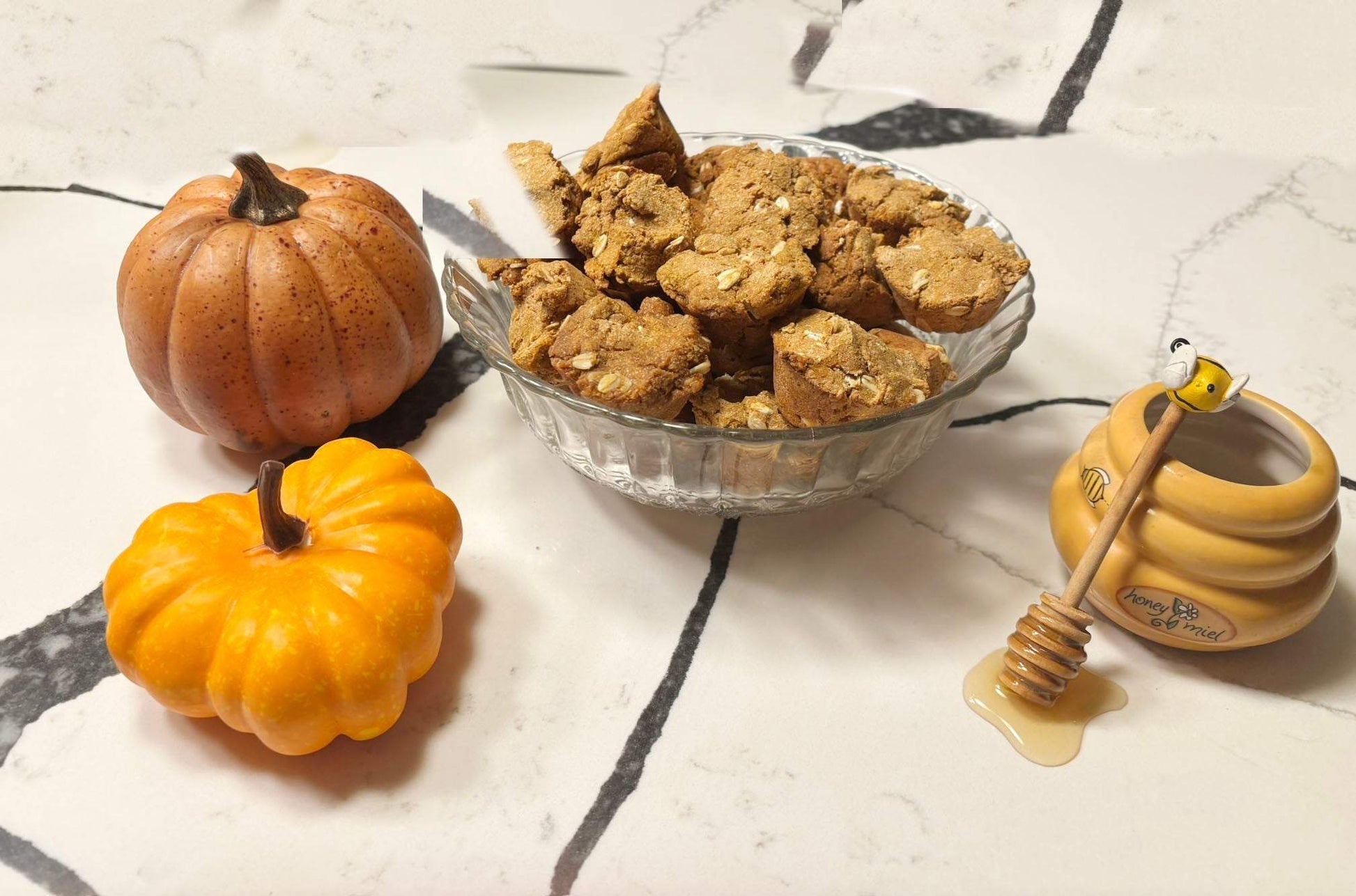 Organic pumpkin muffins for dogs with human-grade ingredients in glass bowl, pumpkins and honey pot on marble surface