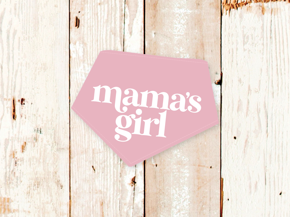 Pink "Mama's Girl" dog bandana with white text and adjustable snap closures on wooden background
