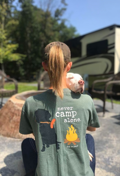 Green "Never Camp Alone" t-shirt featuring dog and campfire graphics, worn outdoors