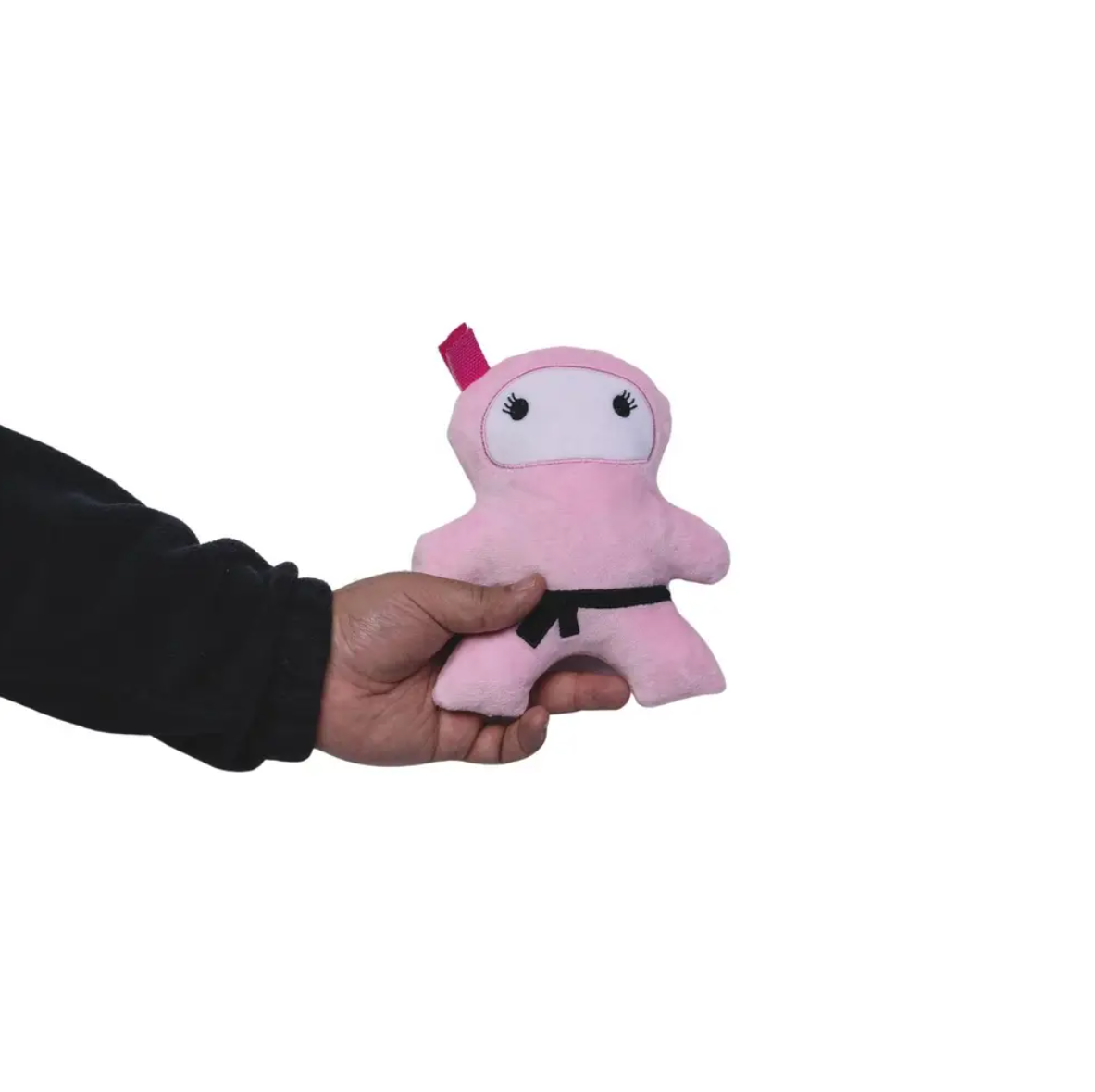 Hand holding pink plush ninja dog toy with black belt and eyes against white background
