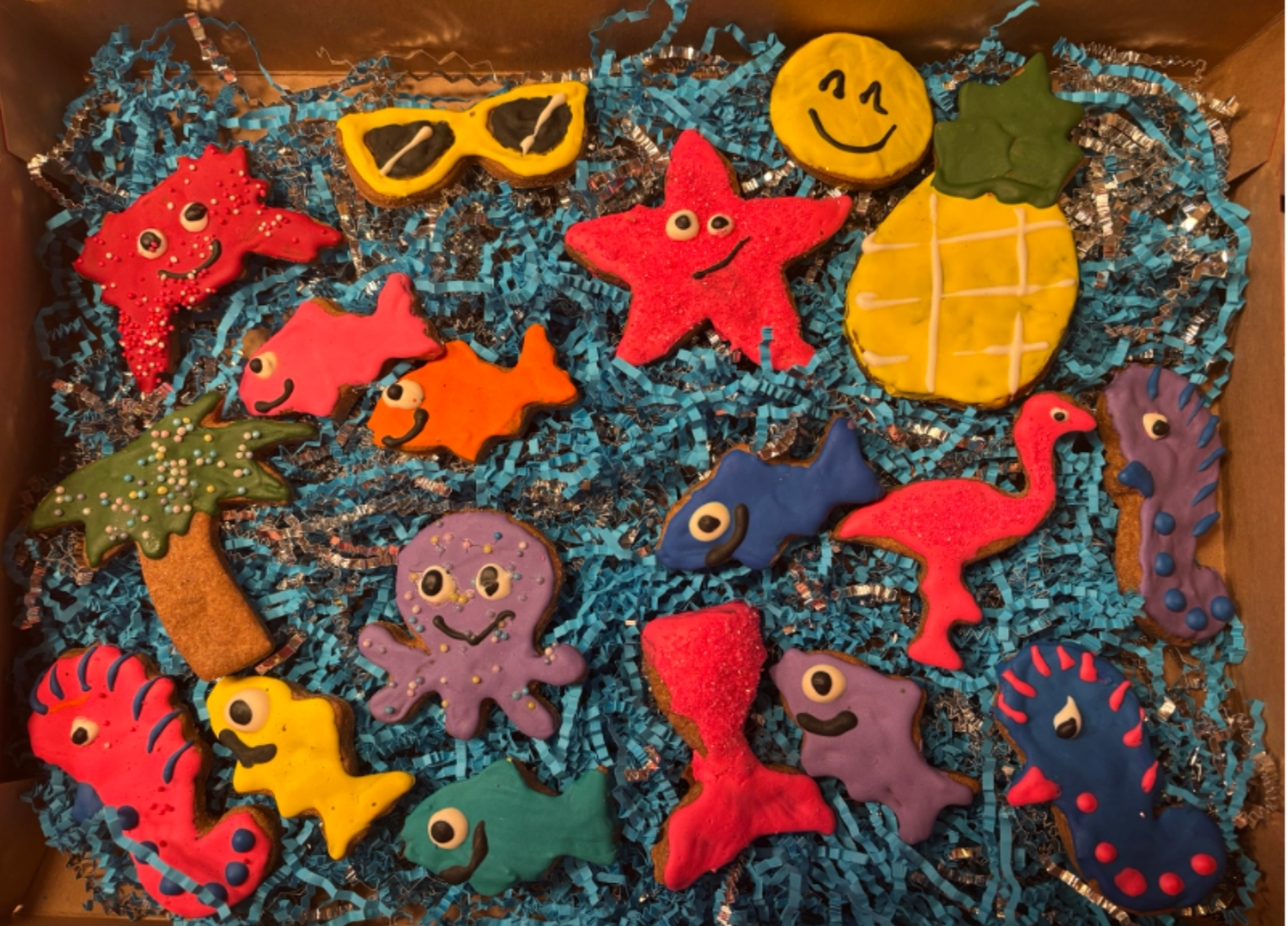PAWaquarium Dog Cookie Box with colorful ocean-themed organic dog cookies including starfish, fish, octopus, pineapple, palm tree, flamingo, and sunglasses designs in a pink gift box