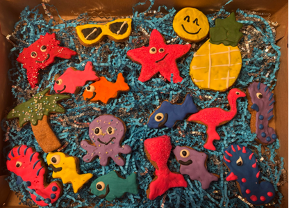 PAWaquarium Dog Cookie Box with colorful ocean-themed organic dog cookies including starfish, fish, octopus, pineapple, palm tree, flamingo, and sunglasses designs in a pink gift box