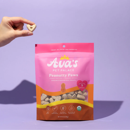 Ava's Pet Palace organic peanut butter dog treats in pink and orange packaging with hand holding heart-shaped treat against purple background