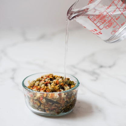 Pouring water into a bowl of grain free dog food premix on marble surface