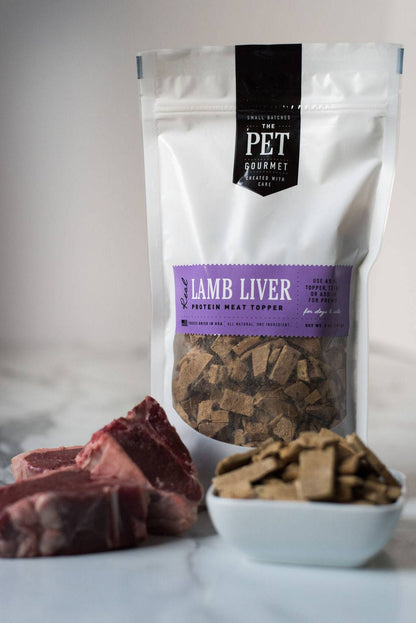 Freeze dried lamb liver dog treat protein meat topper in white resealable pouch with fresh meat pieces and bowl of treats on table
