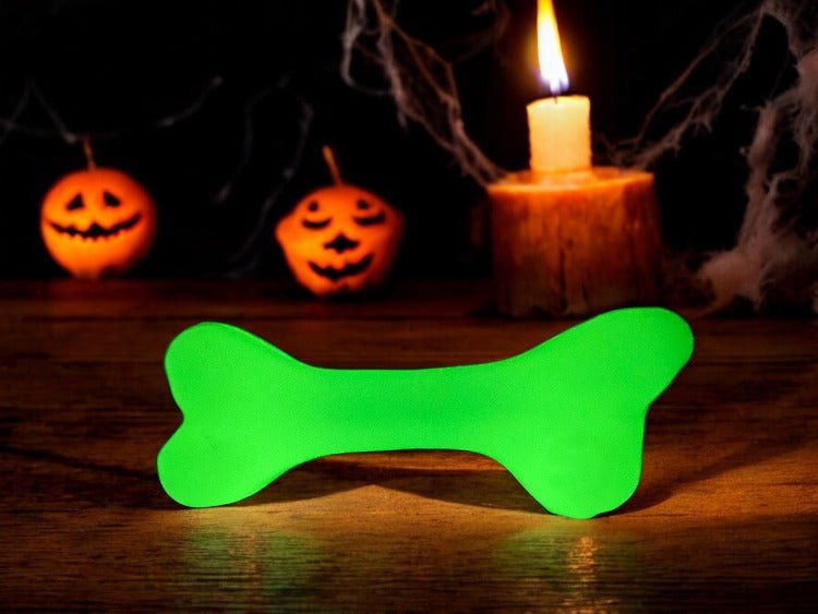 Glow-in-the-dark green rubber bone dog toy glowing near candle and Halloween pumpkins