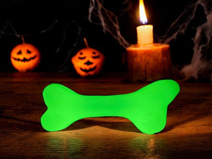 Glow-in-the-dark green rubber bone dog toy glowing near candle and Halloween pumpkins