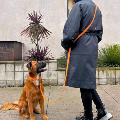 Person wearing black coat walking dog with orange PVC handsfree dog leash outdoors