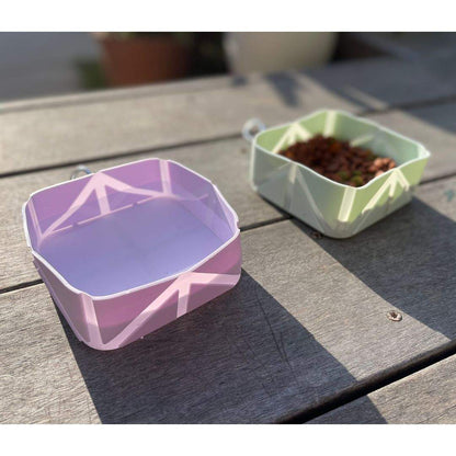 Foldable pet food and water bowls in purple and green on wooden surface for travel use