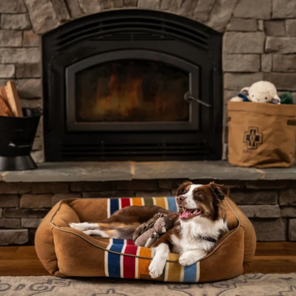 Pendleton National Park Kuddler cozy dog bed with colorful stripes and plush filling next to fireplace