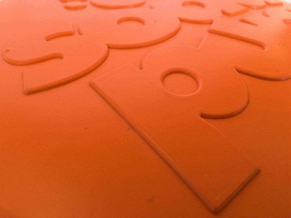 Close-up of orange durable rubber Bottle Top Flyer dog frisbee with embossed design