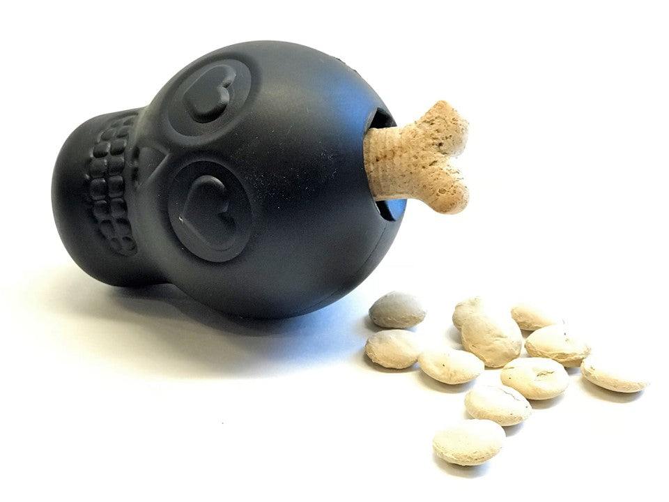 Magnum Sugar Skull black chew toy and treat dispenser with bone-shaped treat and kibble pieces scattered nearby