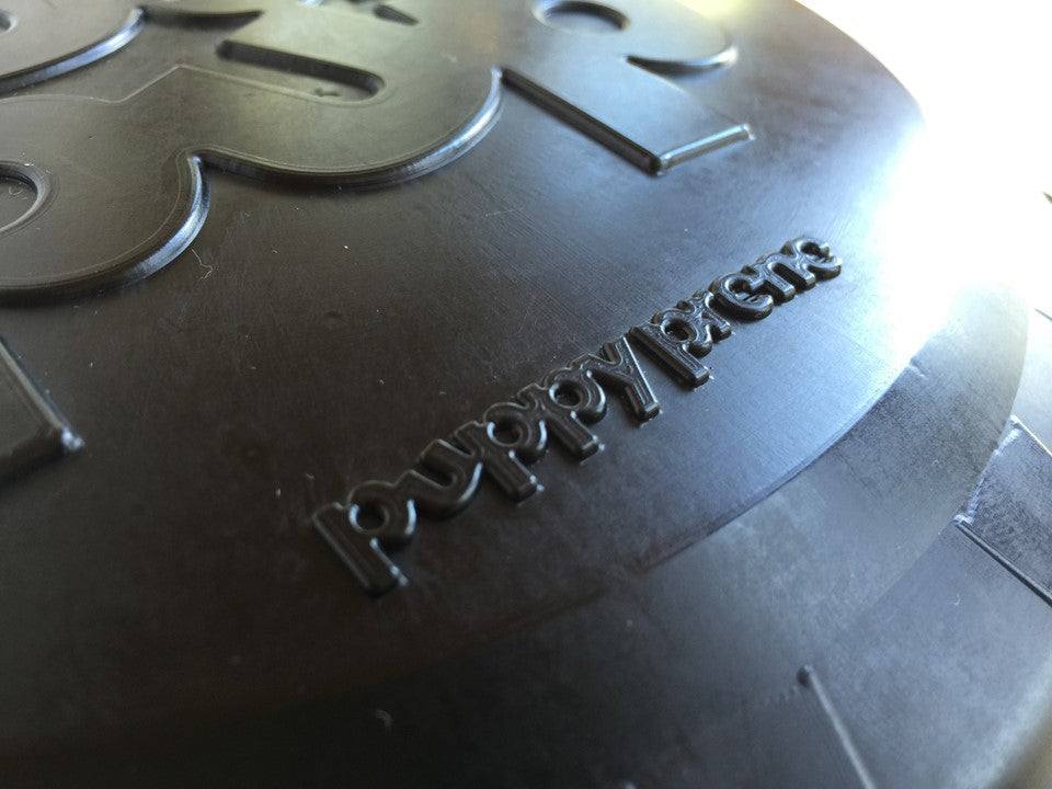 Large black Magnum Bottle Top Flyer durable rubber dog retrieving frisbee close-up with embossed text puppy gymnastics