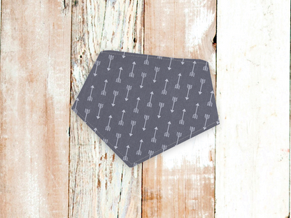Grey dog bandana with white arrow pattern and adjustable snap closures on wooden background