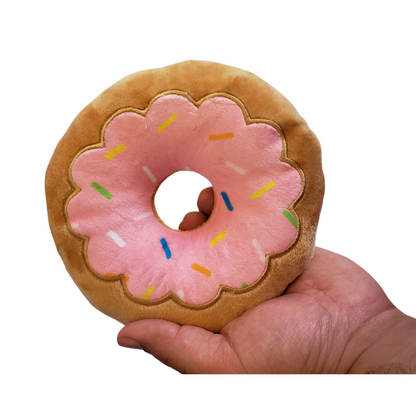 Strawberry donut plush dog toy held in hand, soft and durable for chewing and play