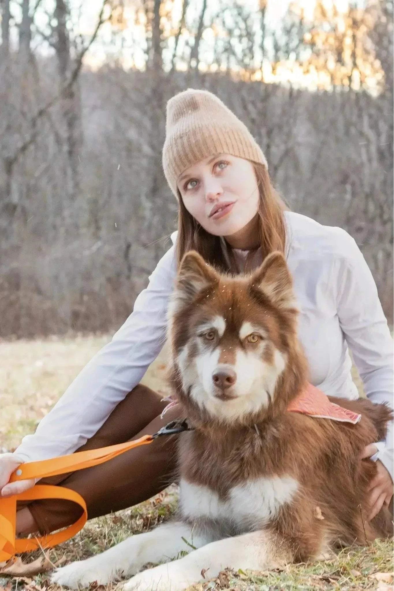 Dog wearing Twilight Trails Bandana and orange leash with woman in beanie outdoors