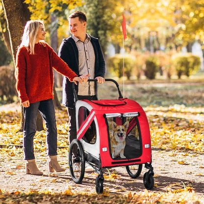 Couple walking with a red 2-in-1 pet bike trailer stroller carrying a small dog on a leafy park path