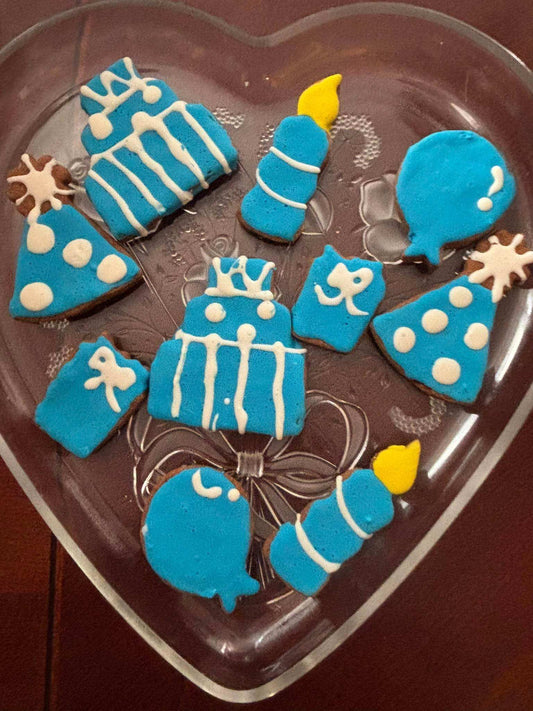 Birthday Boy Organic Dog Cookie Box featuring blue and white iced peanut butter cookies shaped like balloons, party hats, candles, presents, and cakes