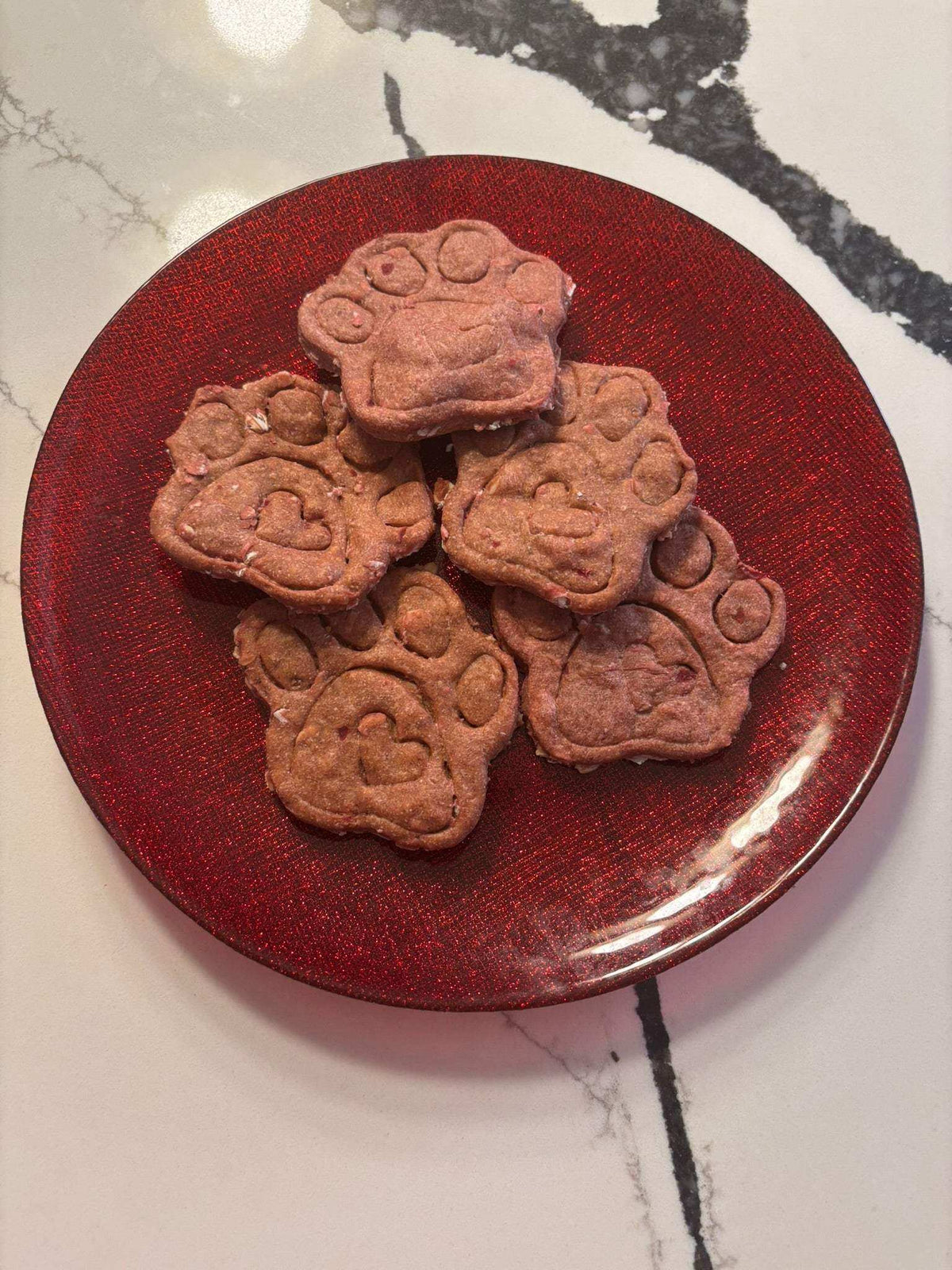 Crunchy Beet-a-licious Paws organic dog treats in vibrant red paw shapes with a crunchy texture on a red plate