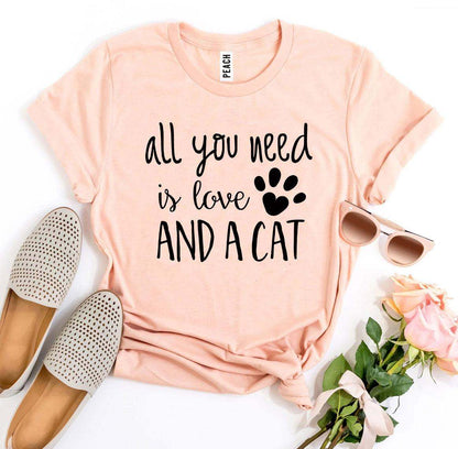 Peach All You Need Is Love And a Cat T-Shirt with black text and paw print design, styled with sunglasses, shoes, and flowers