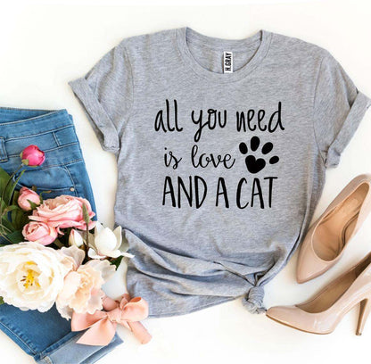 Grey "All You Need Is Love And A Cat" t-shirt with paw print design, paired with blue jeans, flowers, and beige heels