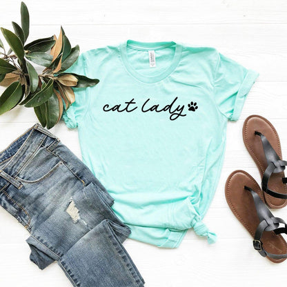 Light blue Cat Lady T-Shirt with black text and paw print, paired with ripped jeans and sandals on white background