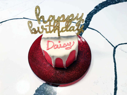 Dog Birthday Gotcha Cake with white dog-friendly frosting and pink base on red glittery plate with golden happy birthday topper