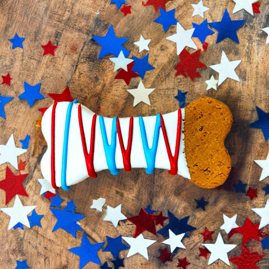 Dipped Bones dog treat with patriotic red, white, and blue icing on wooden surface with star-shaped confetti